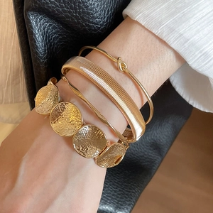 Detail of four-piece gold cuff bracelet set showing varied textures on a model's wrist