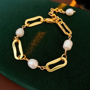 Close-up of gold-plated paperclip chain bracelet with freshwater pearls on green velvet