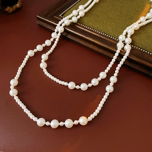 Detail of layered pearl necklace draped over brown leather and green wooden frames