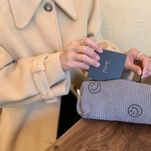 Macro shot of grey corduroy makeup bag with embroidered smiley face on wooden surface