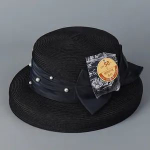 Detail of black straw sun hat with UPF 50+ protection, pearl bow, and plant fiber weave