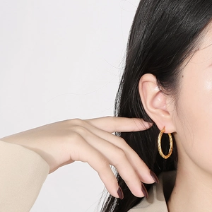 Dettaglio dell'orecchino a cerchio intrecciato dorato da 30mm indossato da una modella