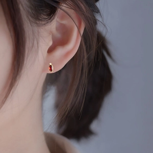 Close-up of minimalist gold ruby stud earrings with small diamond on female model