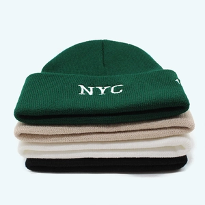 Detail of stacked knitted beanies in green, khaki, beige, and black with NYC embroidery