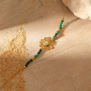 Detail of gold flower pendant with green stone on natural stone background