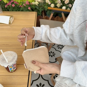 Gros plan d'une mini pochette beige gaufrée avec fermeture éclair et dragonne au café