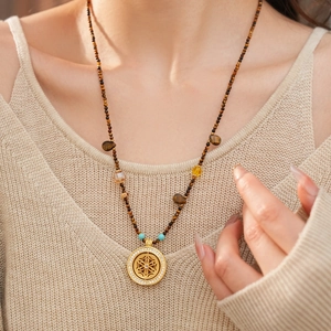 Detail of tiger eye beaded necklace with gold openwork pendant on beige knitwear