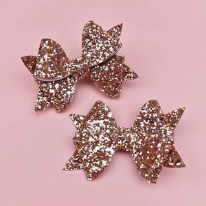 Detailed view of two rose gold sequined glitter bow clips on a soft pink background