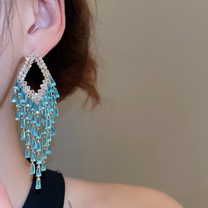 Close-up of model wearing gold tassel earrings with sparkling blue rhinestones
