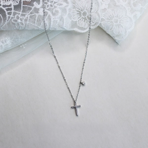 Detail of silver S925 cross necklace with sparkling crystals on white lace background