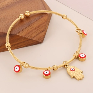 Detail of 18K gold-plated twisted cable cuff featuring red evil eye charms and Hamsa pendant