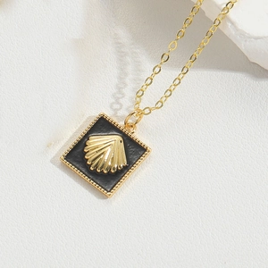 Close-up of golden necklace pendant with a 3D shell motif on a black square background