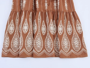 Détail de broderies bohèmes blanches et textures plissées sur une robe longue marron
