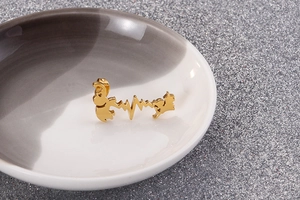 Detail of gold heartbeat and animal silhouette stud earrings on a round display dish