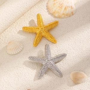Macro shot of gold and silver starfish jewelry with pavé crystals on beach sand
