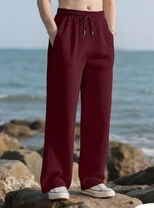Detail of burgundy ribbed knit trousers with drawstring waist on outdoor rocky background