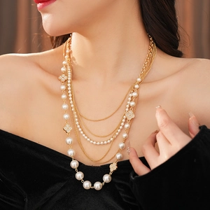 Detail of layered gold necklace with pearls and clover motifs worn on model