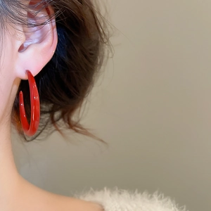 Close-up of elegant red resin C-shape stud earrings worn by a model in profile view
