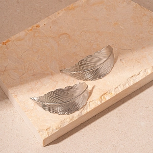 Detailed view of silver leaf stud earrings with realistic textures on a stone surface