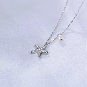 Detail of silver starfish pendant with sparkling diamonds and white pearl on soft fabric