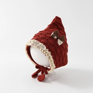 Detail of red knit baby elf hat with lace trim and bow accent on model stand
