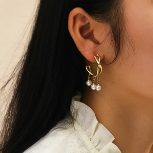 Close-up of golden twisted hoop earrings with three white pearl drops on a model