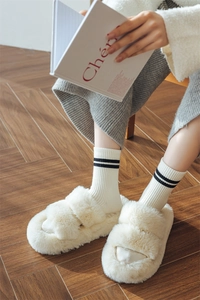 Cosy white fuzzy slide slippers with double straps on wooden floor in warm natural light