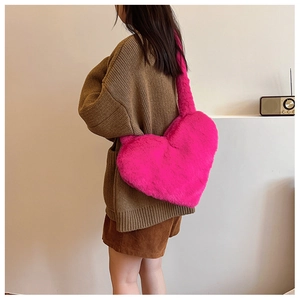 Detail of bright pink heart-shaped plush shoulder bag worn by model in a natural setting