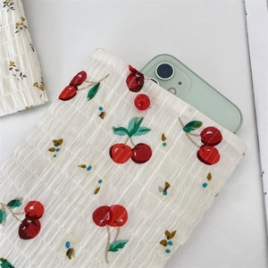 Dettaglio di una borsa con stampa a ciliegie che contiene uno smartphone verde