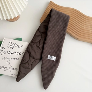Detail of dark brown quilted scarf with diamond stitching and label on white surface