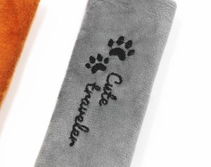 Detalle de protector de cinturón de felpa gris con bordado Cute Traveler y huellas de patas