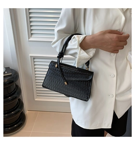 Close-up of black textured shoulder bag with gold metal buckle and vertical grain detail