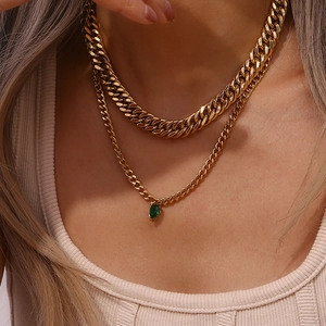 Detail of layered gold cuban chain necklace with a green pear-shaped zircon pendant