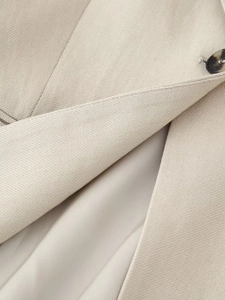 Close-up of beige sleeveless vest showing woven fabric texture and brown button detail