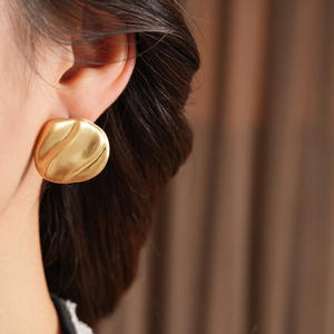 Close-up of golden matte geometric earrings on model showing size and brushed metal texture