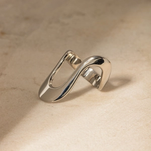 Detail showing wave-shaped open ring in silver finish on a textured stone surface
