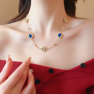Close-up of gold chain necklace with blue clover and diamond-shaped charms on model