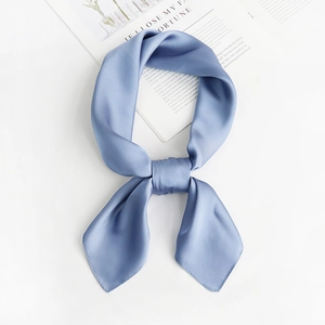 Close-up of a blue silk square scarf knotted on a magazine over a white background