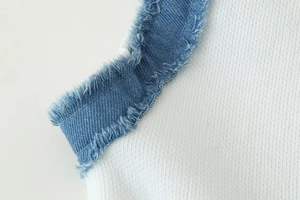 Détail de maille blanche cousue avec une bordure en jean bleu effiloché