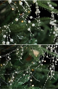 Detail of white and silver pearl bead garland draped on green Christmas tree branches