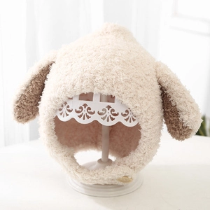 Cute beige plush baby winter hat with floppy brown ears shown on a white display stand