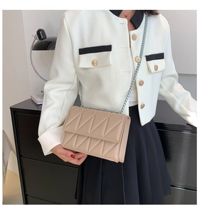 Detail of beige geometric quilted flap bag with silver chain strap on a black cabinet