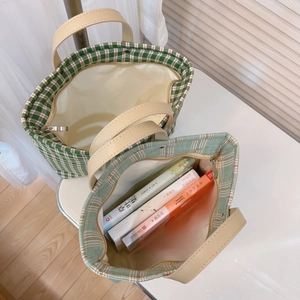 Green checkered tote bag with leather handles and zip closure shown with books inside