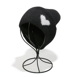 Detailed view of the black knit beanie with a white fuzzy heart patch on the side