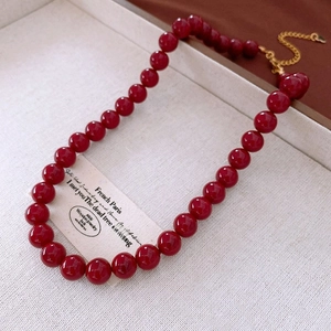 Close-up of deep red beaded necklace with golden heart pendant on woven background