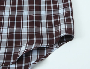 Detail of curved hem on brown and blue plaid shirt with precise stitching and seams
