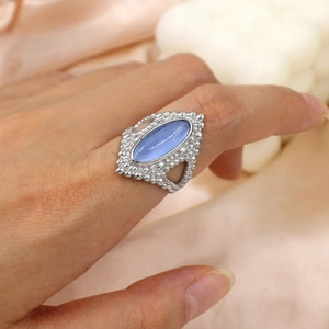Vintage silver ring with oval blue gemstone worn on finger over pink silk background