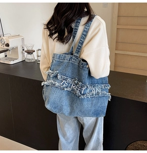 Détail d'un sac cabas en denim bleu avec bords effilochés et logo 7STREET LANE brodé