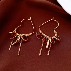 Detail of 18K gold-plated heart earrings with red glass droplets and metal tassels