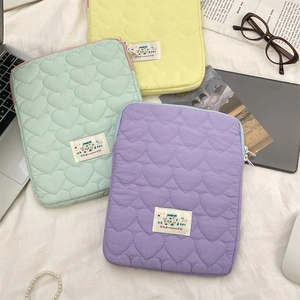 Flat lay of heart-quilted laptop sleeves in yellow, mint, and purple with lifestyle props